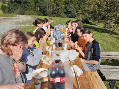 Eine Gruppe von Menschen isst und trinkt gemeinsam an einem langen Picknicktisch im Freien.