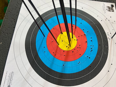 Bogenschießziel mit mehreren Pfeilen, die in der gelben Mitte und den inneren Ringen gruppiert sind.