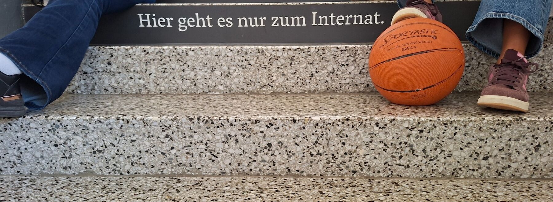 Fünf Menschen sitzen und lächeln in einem gemütlich eingerichteten Schlafsaal mit zwei Betten.